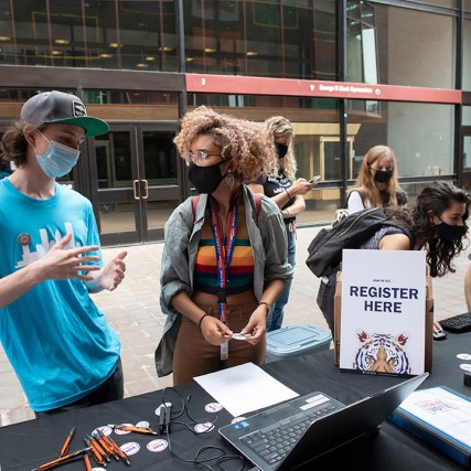 students and staff members at a table outdoors learning about voting registration. 