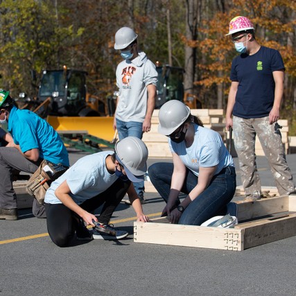 several volunteers building frames for walls of a house in a parking lot.