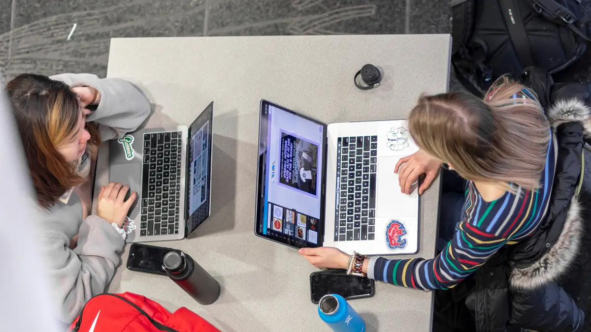 Overhead view of two students working on their laptops while sitting at a table.