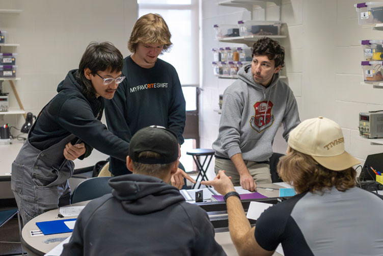 Group of students are working, LA and other two students are standing next to each other