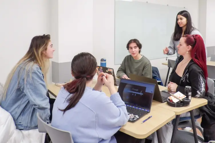 Five RIT students gathered around a couple of desks in a classroom.