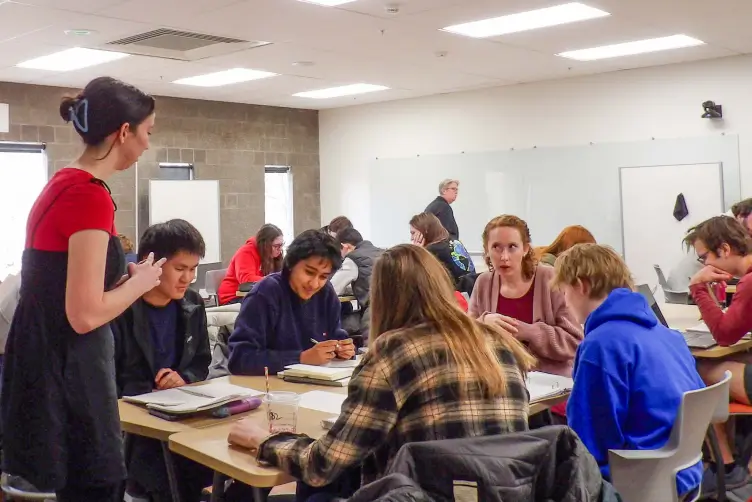 A Learning Assistant standing in front of a group of students in a classroom.
