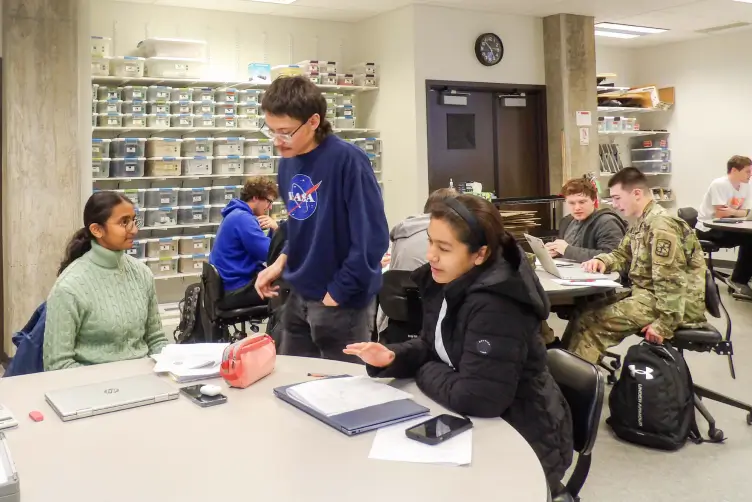 A learning assistant helping a couple of students in a classroom.