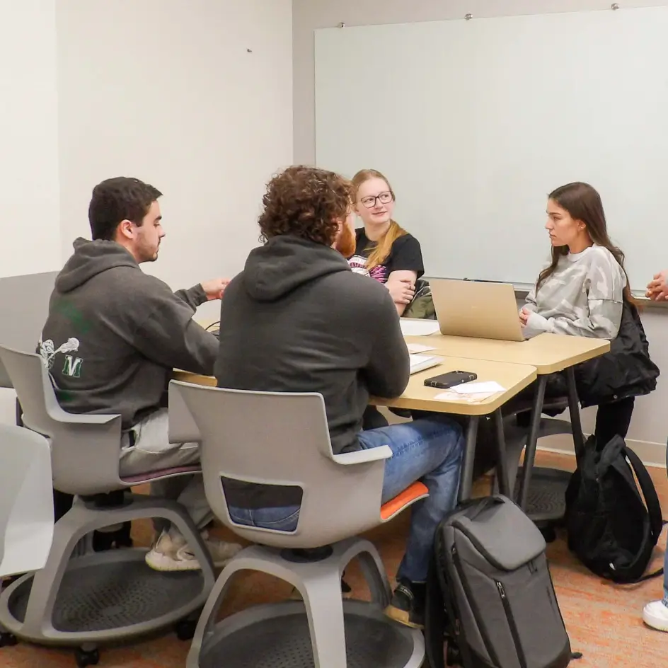 Four students sitting around a couple of tables.