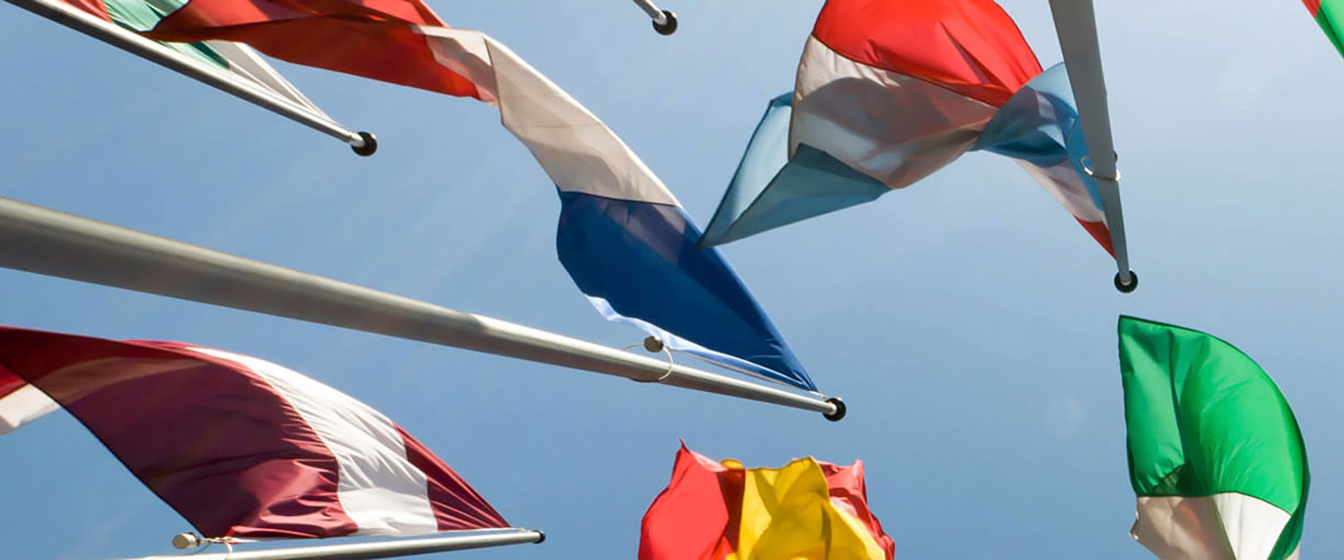 View from below of a variety of flags and blue sky.