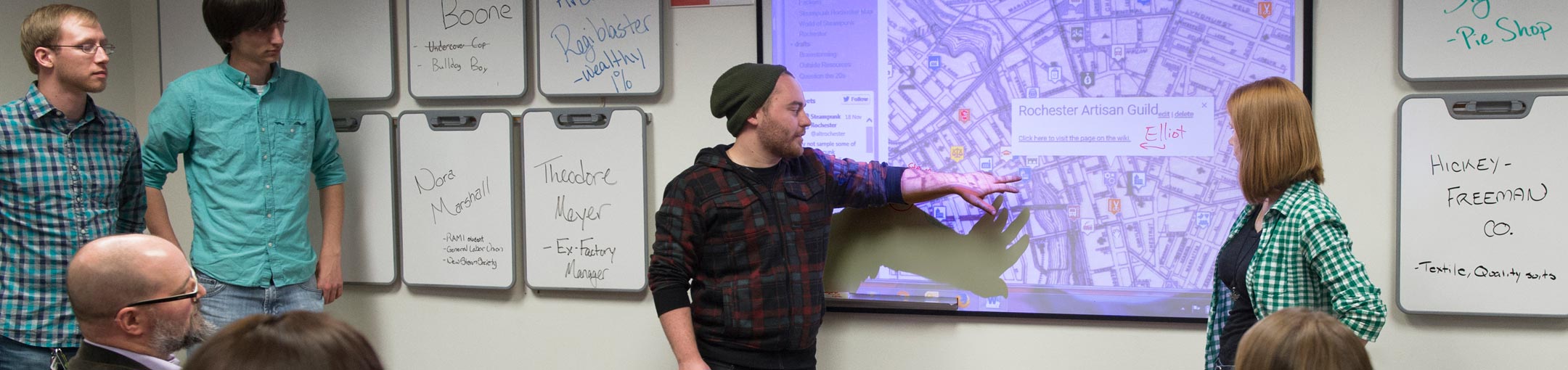 Student giving a presentation using a projector, pointing to an image of a Google map