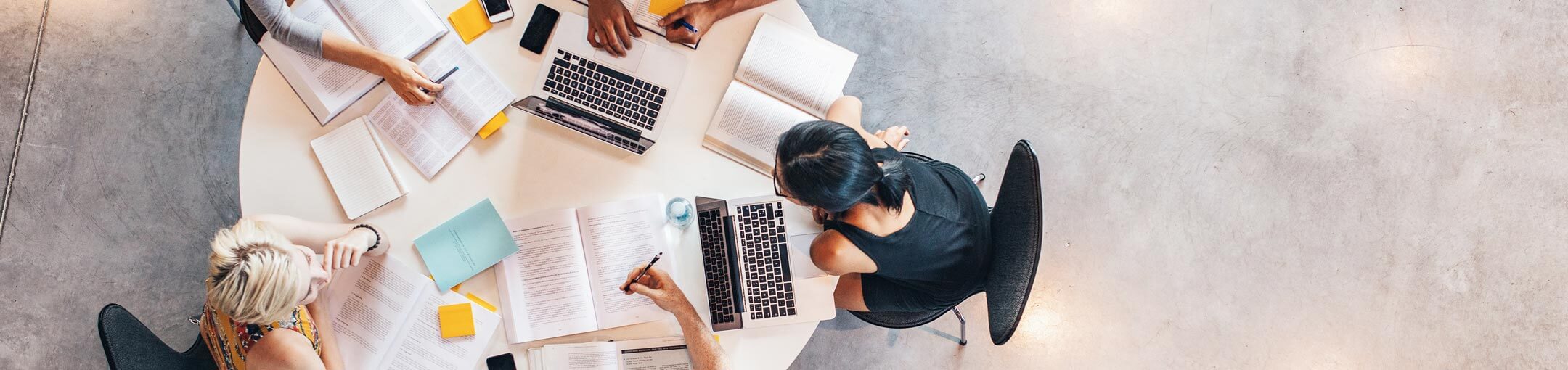 Five people sitting around a table working with books and laptops