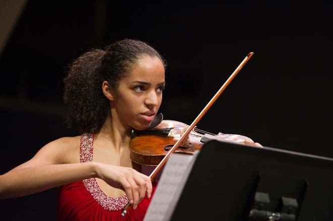 A violinist playing a piece of music with a dark backdrop 