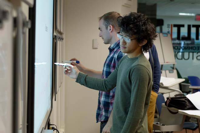 A student and professor working on a white board next to one another