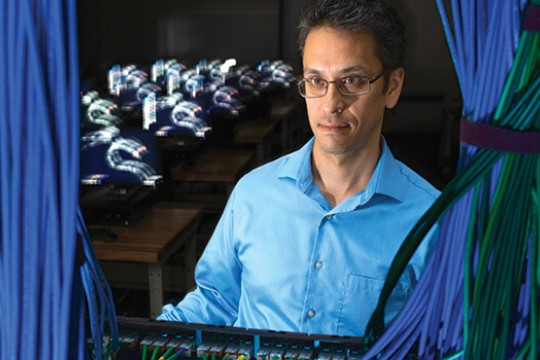 Matthew Wright sits and works on a computer, a bunch of wires bound together framing the photo.