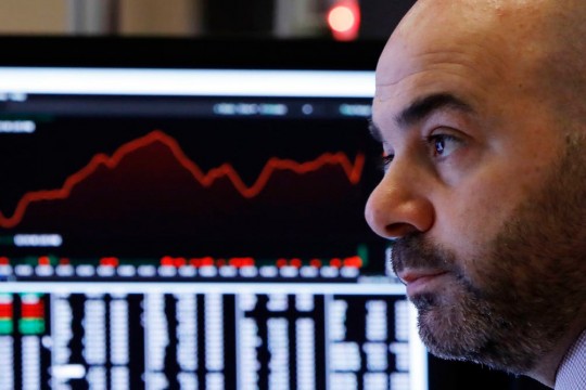 close-up of man's face with computer screen with red line graph in background