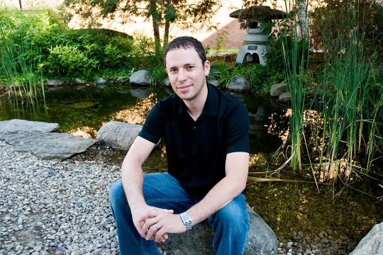 Man sits on rock near pond and garden.