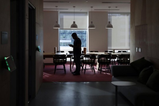 Silhouette of man standing along in dining area lookng at cellphone.