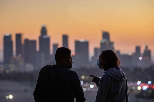 two people wearing masks and talking with a city skyline in the background.