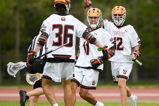 three men's lacrosse players celebrate a goal.