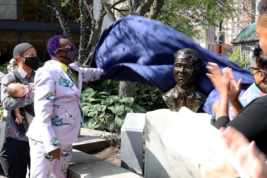 person taking a sheet off of a bronze bust.