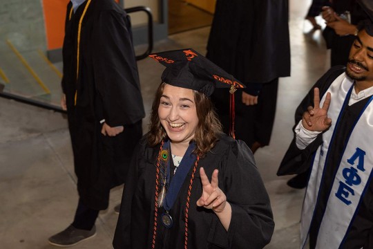 graduate wearing cap and gown and giving the peace sign.