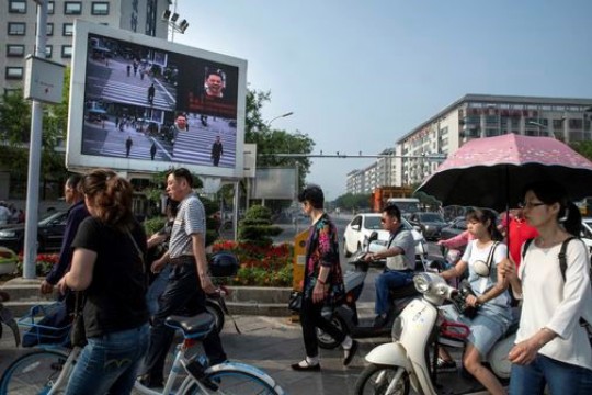 people walking and riding bikes down a street in China.