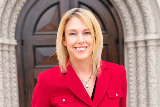 Blonde woman smiling wearing red coat.