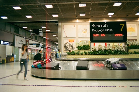 an international baggage claim is featured with a woman entering the frame on the left side.