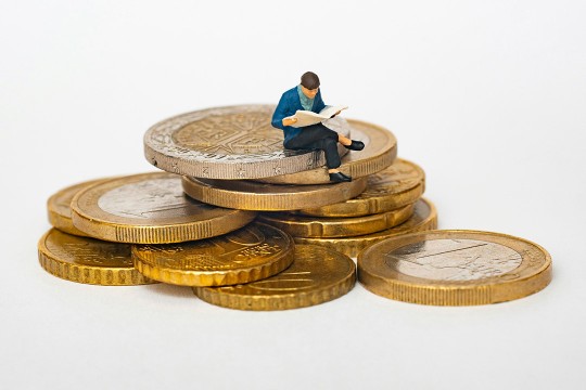 an AI generated model of a miniature man in a suit sitting on top of a pile og giant gold coins on a white background.