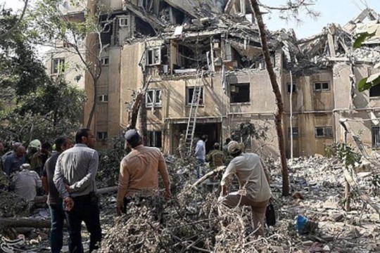 community members in iran look at a destroyed building in Iran.