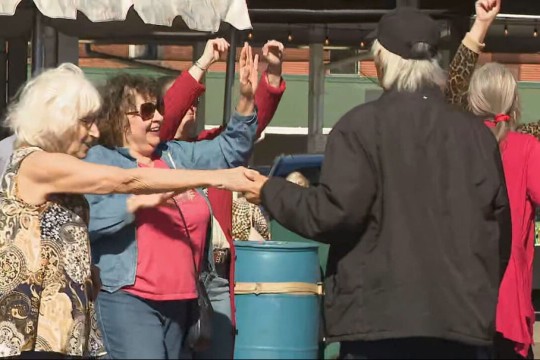 people celebrate italian heritage at the rochester public market by dancing in a circle.