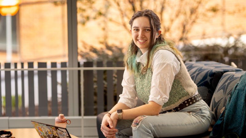 Student sits on a loveseat outside on porch