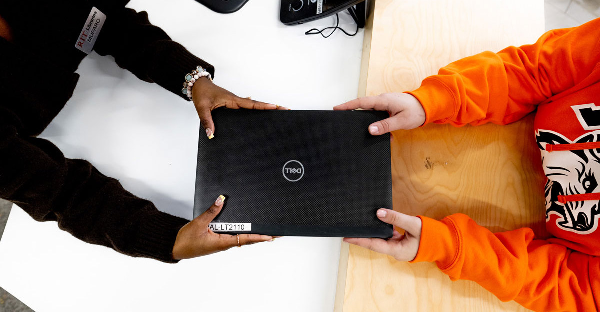 A top view shot of someone anding over a laptop to a student