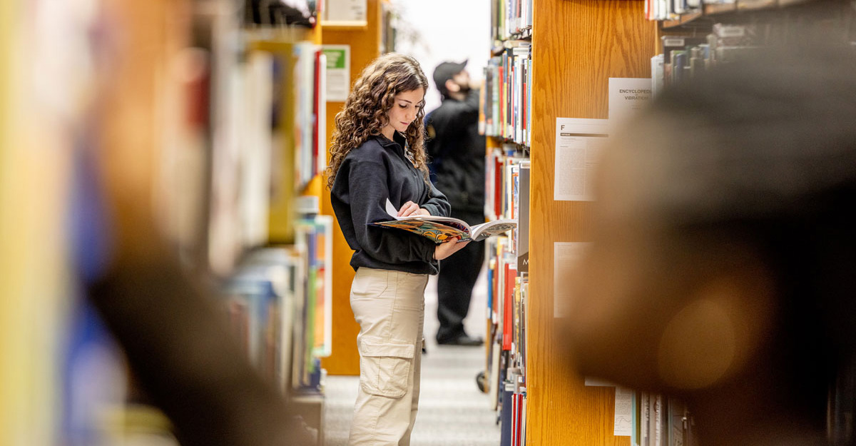 A student in the middle of the book shelves, looking at a book