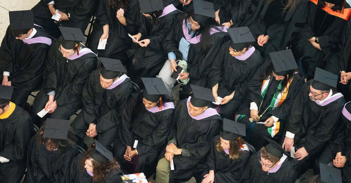 A large crowd of students sitting down at graduation with their graduation garb on.