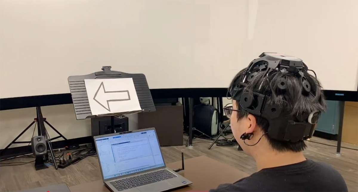 Person wearing a piece of equipment, looking at a laptop screen.