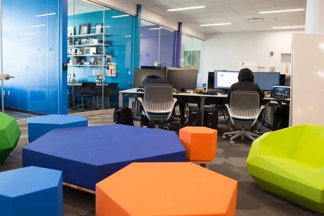 Open room with colorful, hexagonal seats and tables with desktop computers