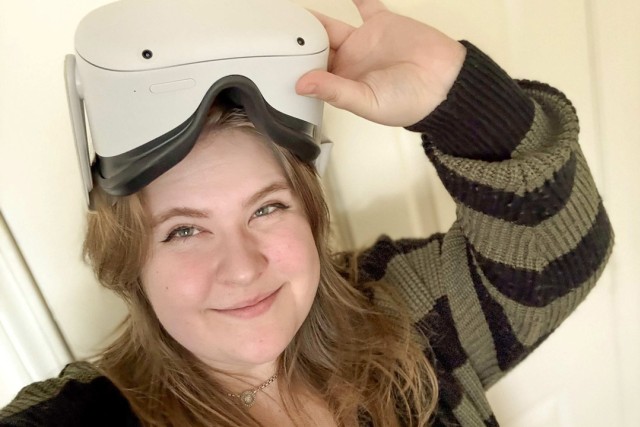 a girl with blonde hair stands with a V R device on her head.