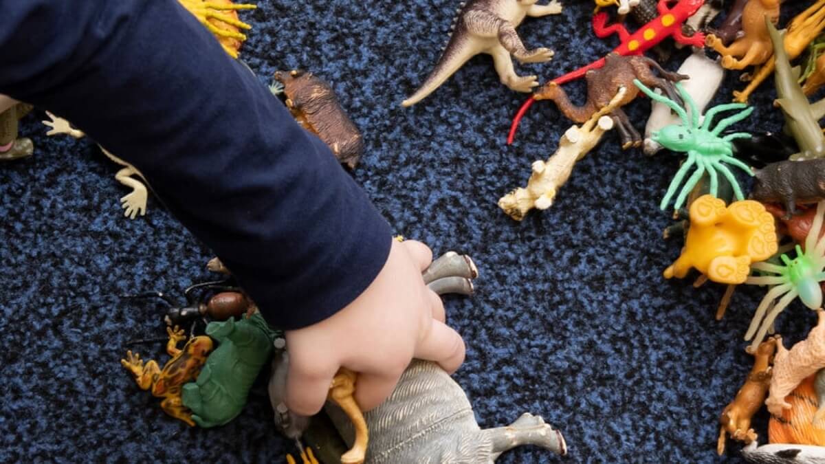A toddler playing with a dinosaur toys on the floor.