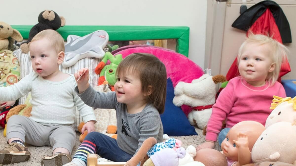 Kids sitting down in a room while teachers read a story to them.
