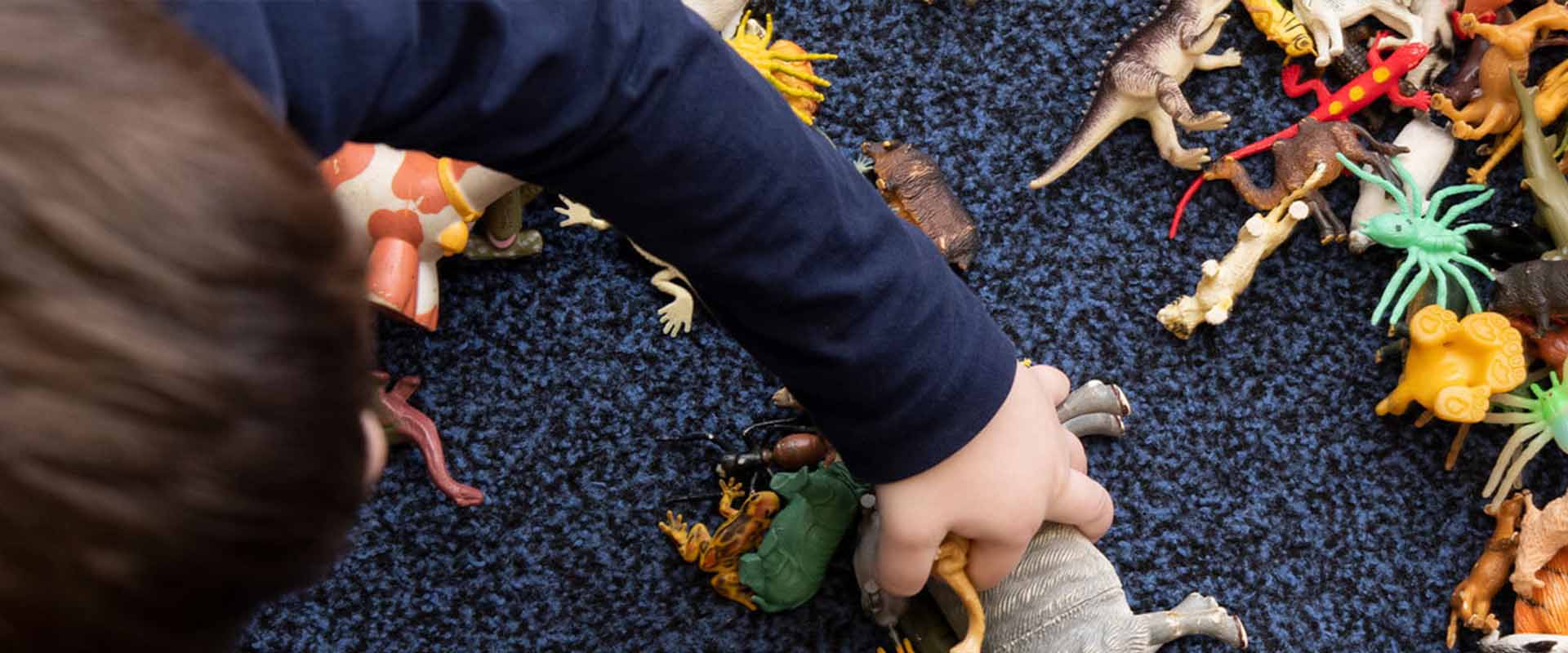 A toddler playing with a dinosaur toys on the floor.