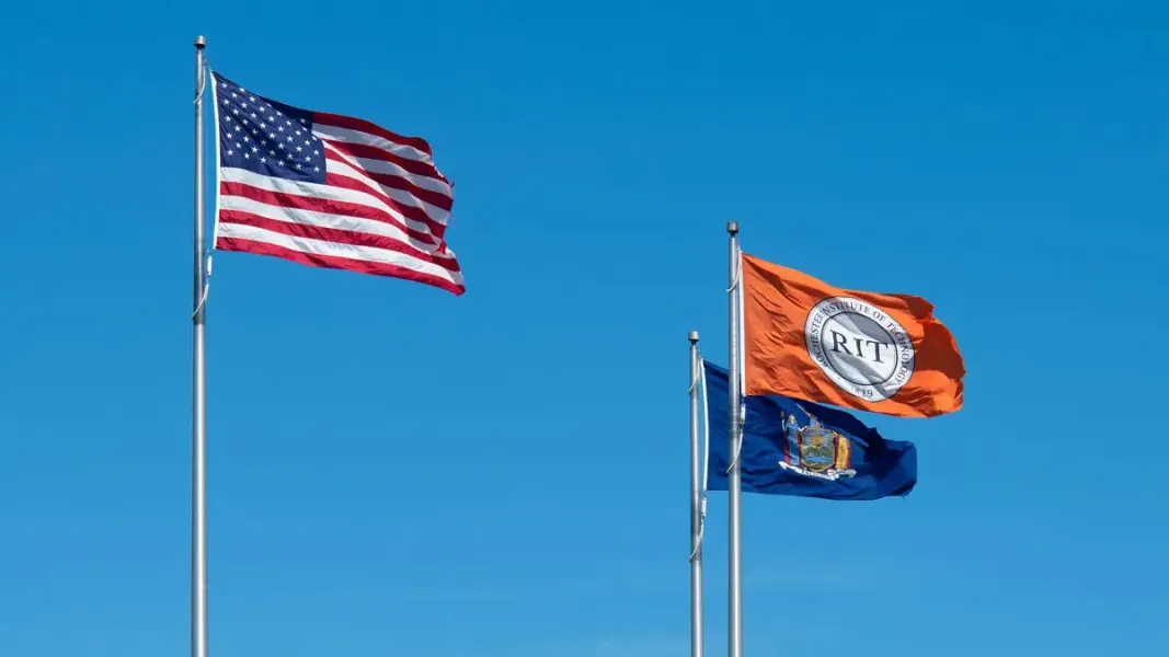 The flags of the United States of America (left), the state of New York (lower right), and R I T (upper right).