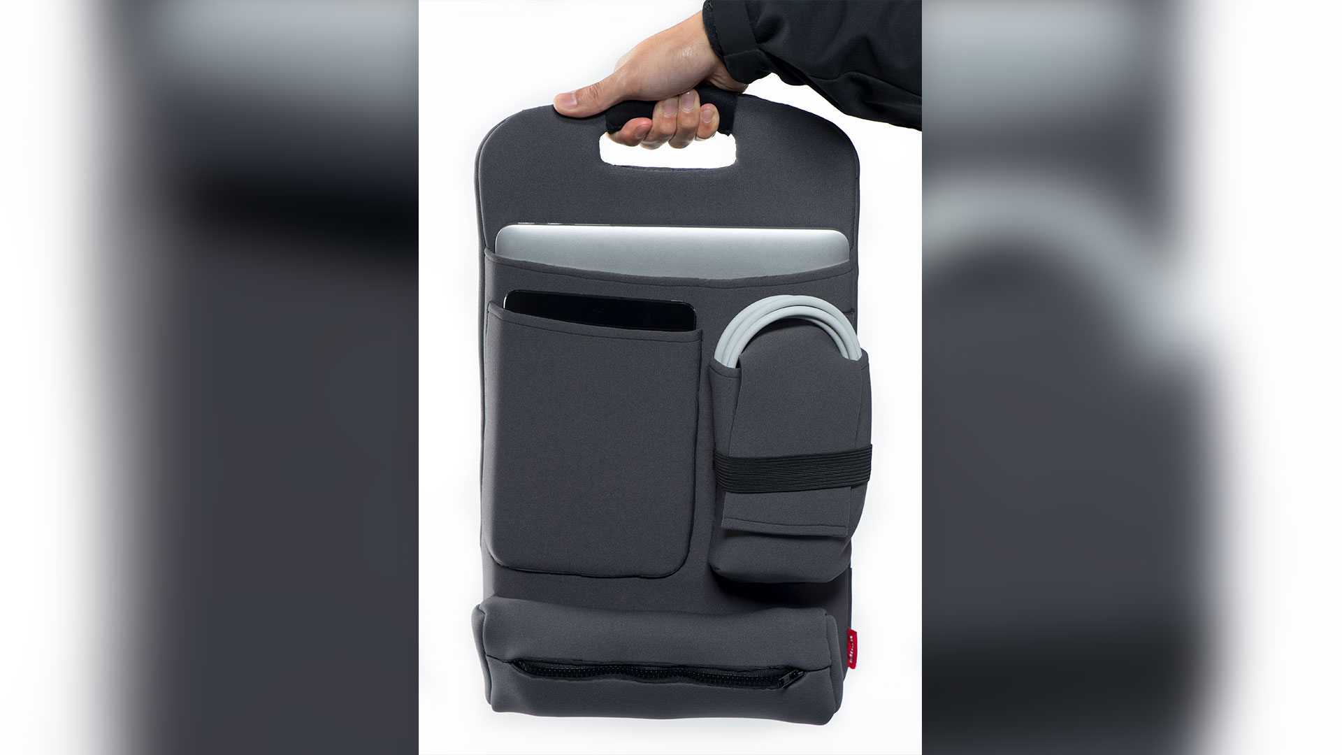 Dark grey backpack organizer standing up being held with handle at top, one large zippered pouch at base two pouches above with an ipad slipped in left side and charging cords on right side and an opening at top below handle showing a laptop in largest compartment