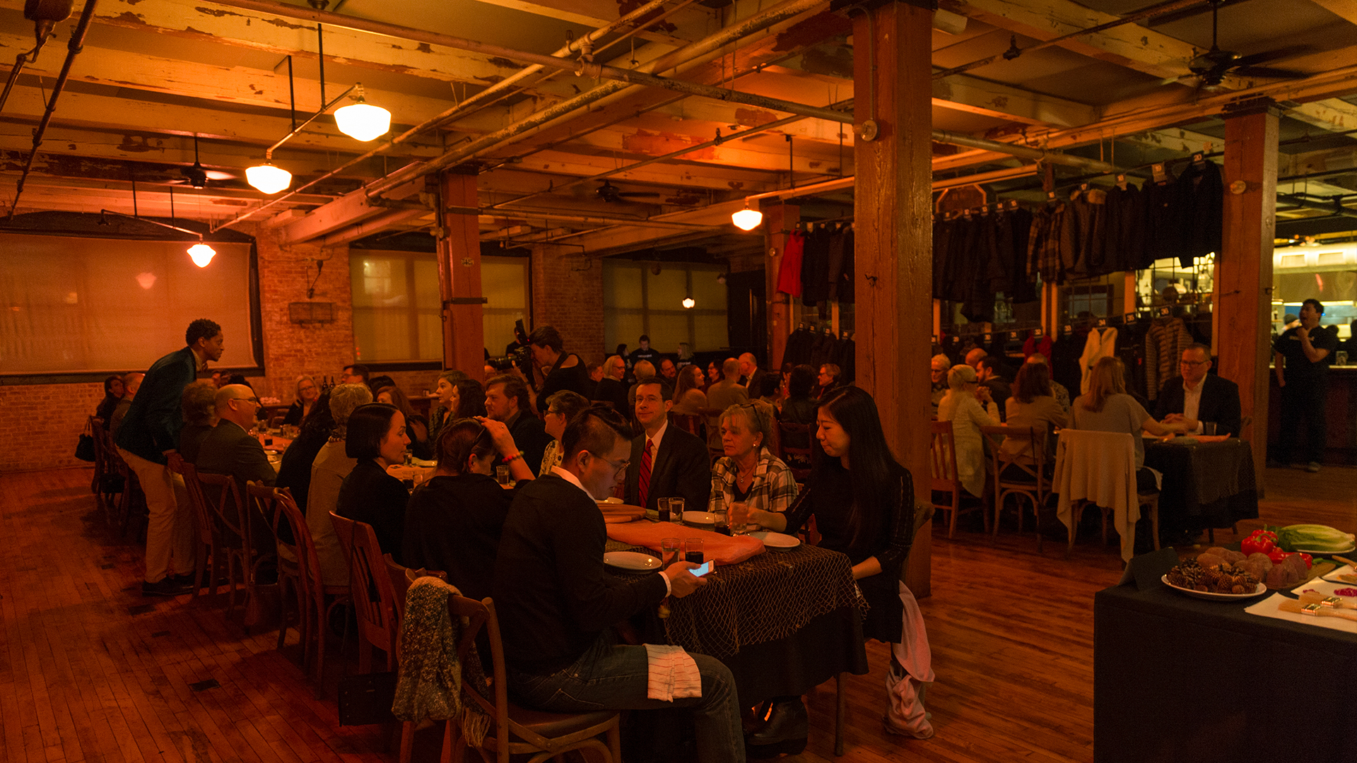 Entire dining event with people seated at tables in a room with warm redish light