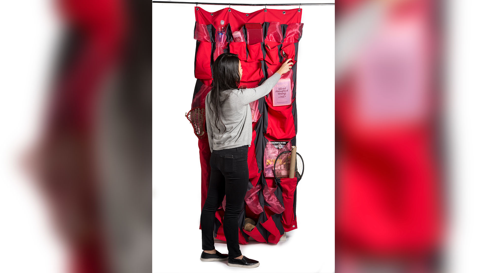 Student standing in front of closet curtain reaching up for item in pocket at top of curtain