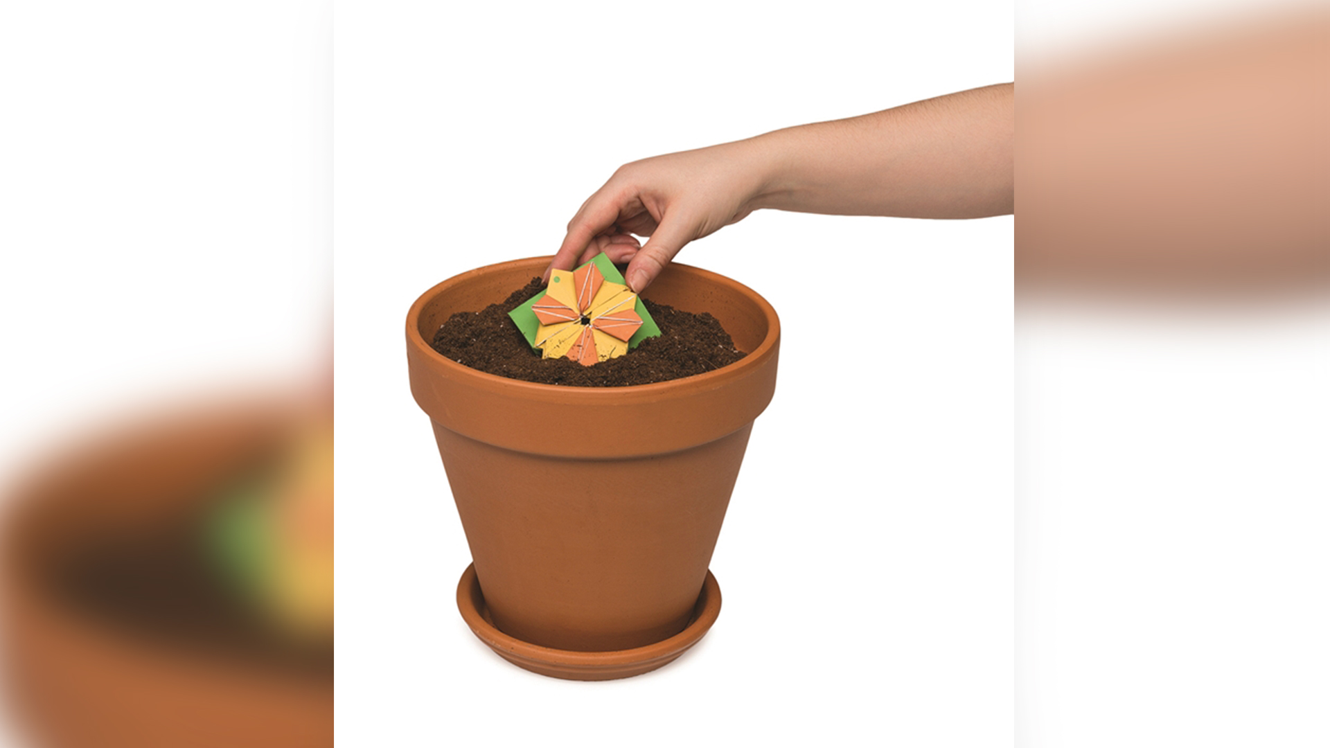Someone placing origami seed packet in soil of flower pot