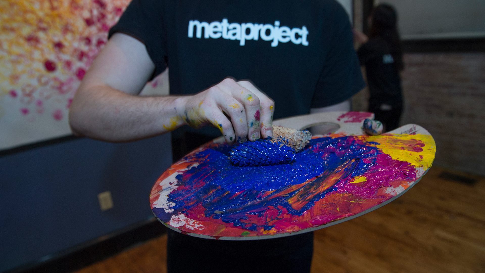 Student holding a paint pallet rolling pine cone in blue paint