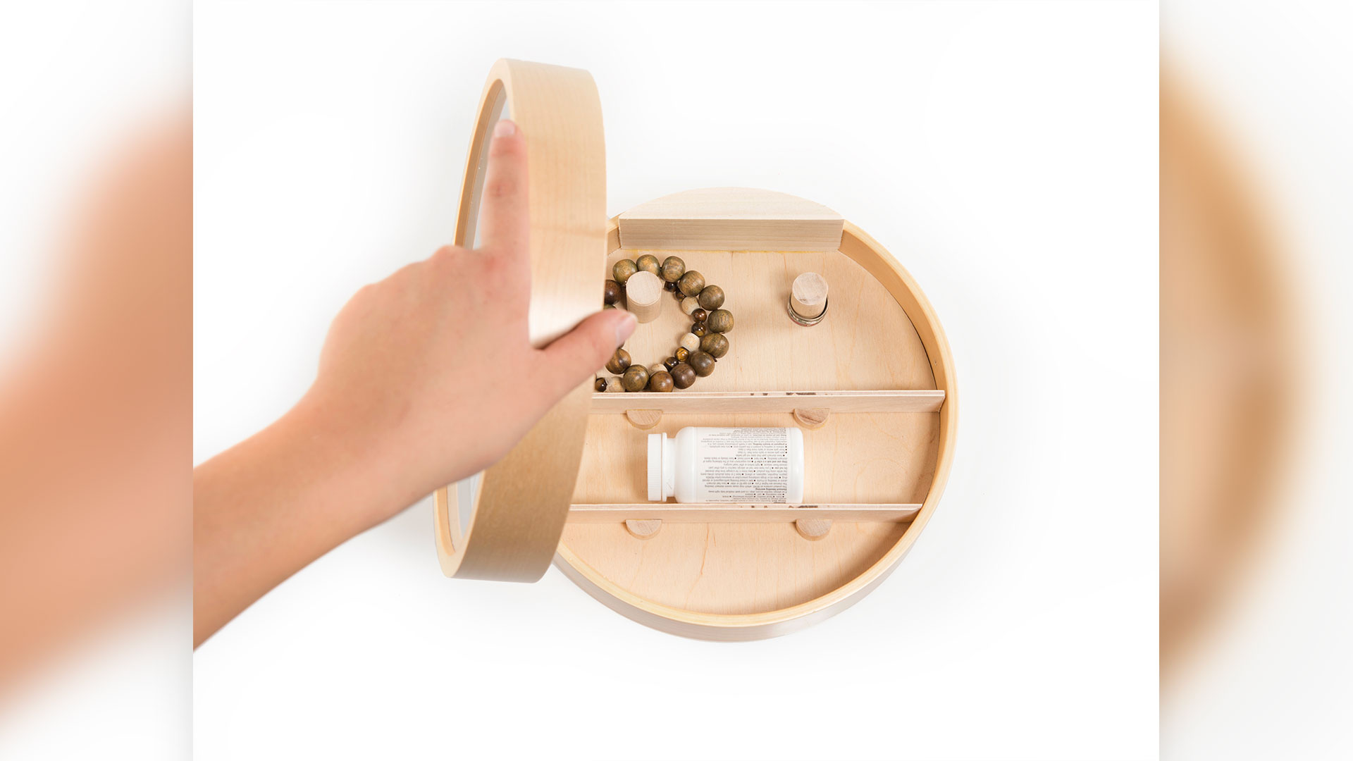 Someone opening up clock face to show 2 interior shelves and two small cylindrical hooks, pill bottle on shelf and small bracelets around cylindrical hooks 