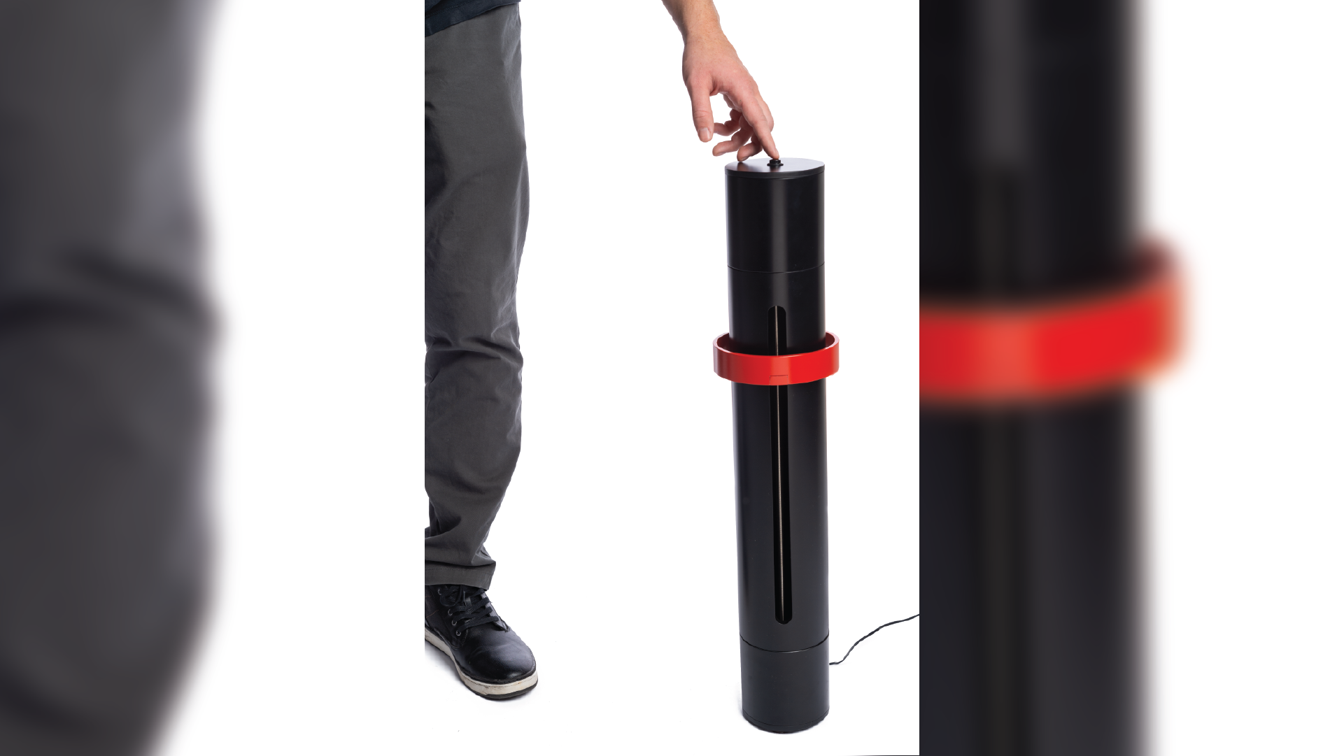 Person standing up right by the clock in a black cylindrical shape with a red ring on it. The person is touching the clock on the top.