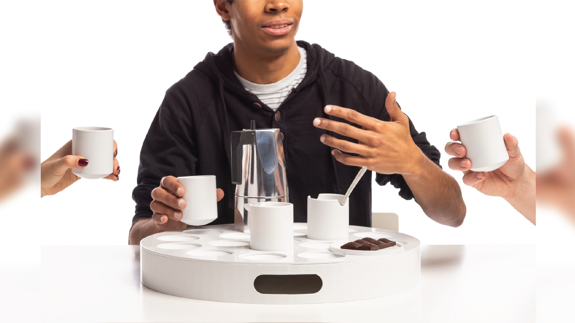 Person interacting on the back ground with hands on the both sides holding cups. The set is in the middle holding some items such as cups, a kettle and food on a tray.