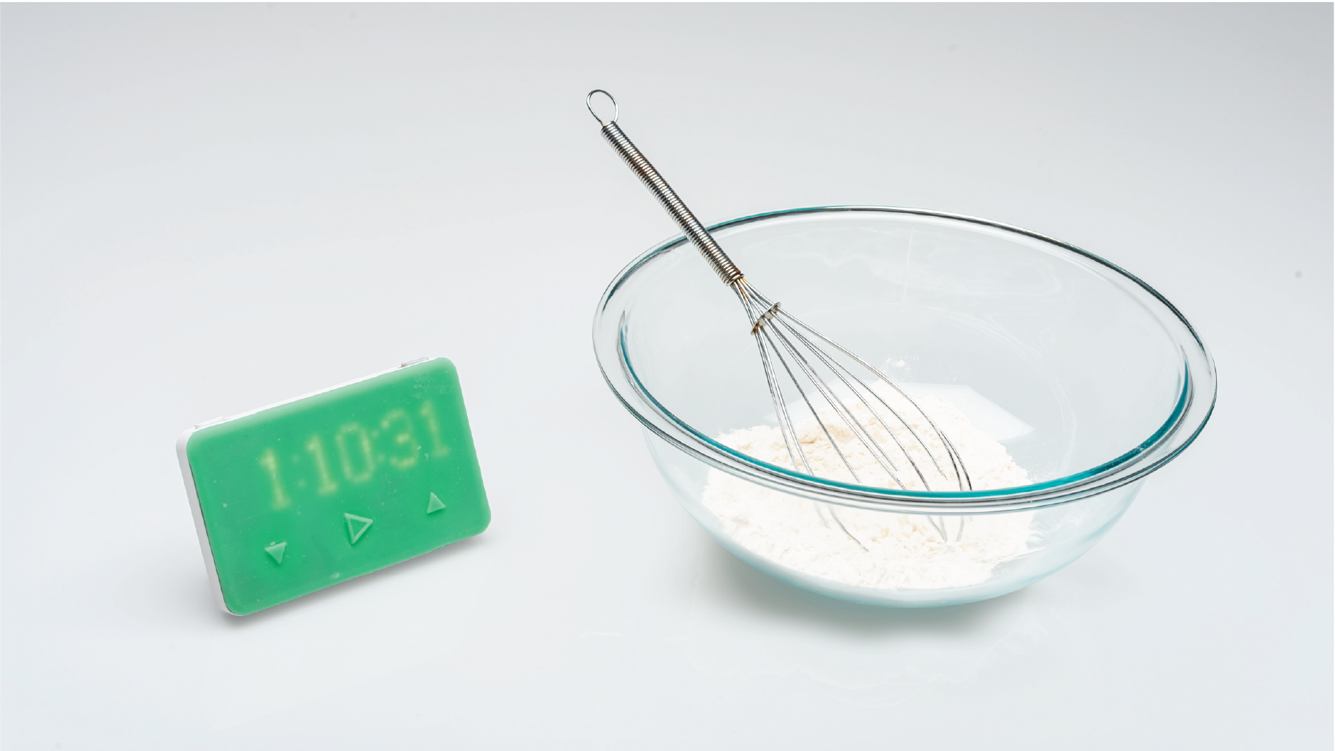 Green timer by side of a bowl with a french whip/whisk.