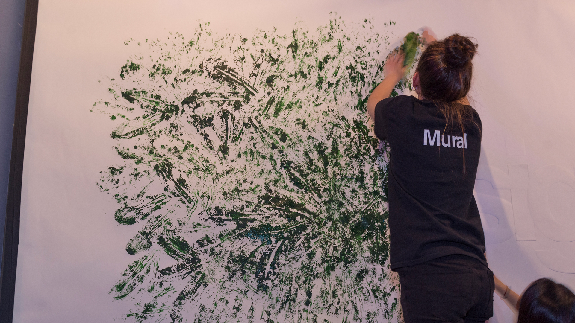 Student using lettuce leaf to stamp green paint on mural wall