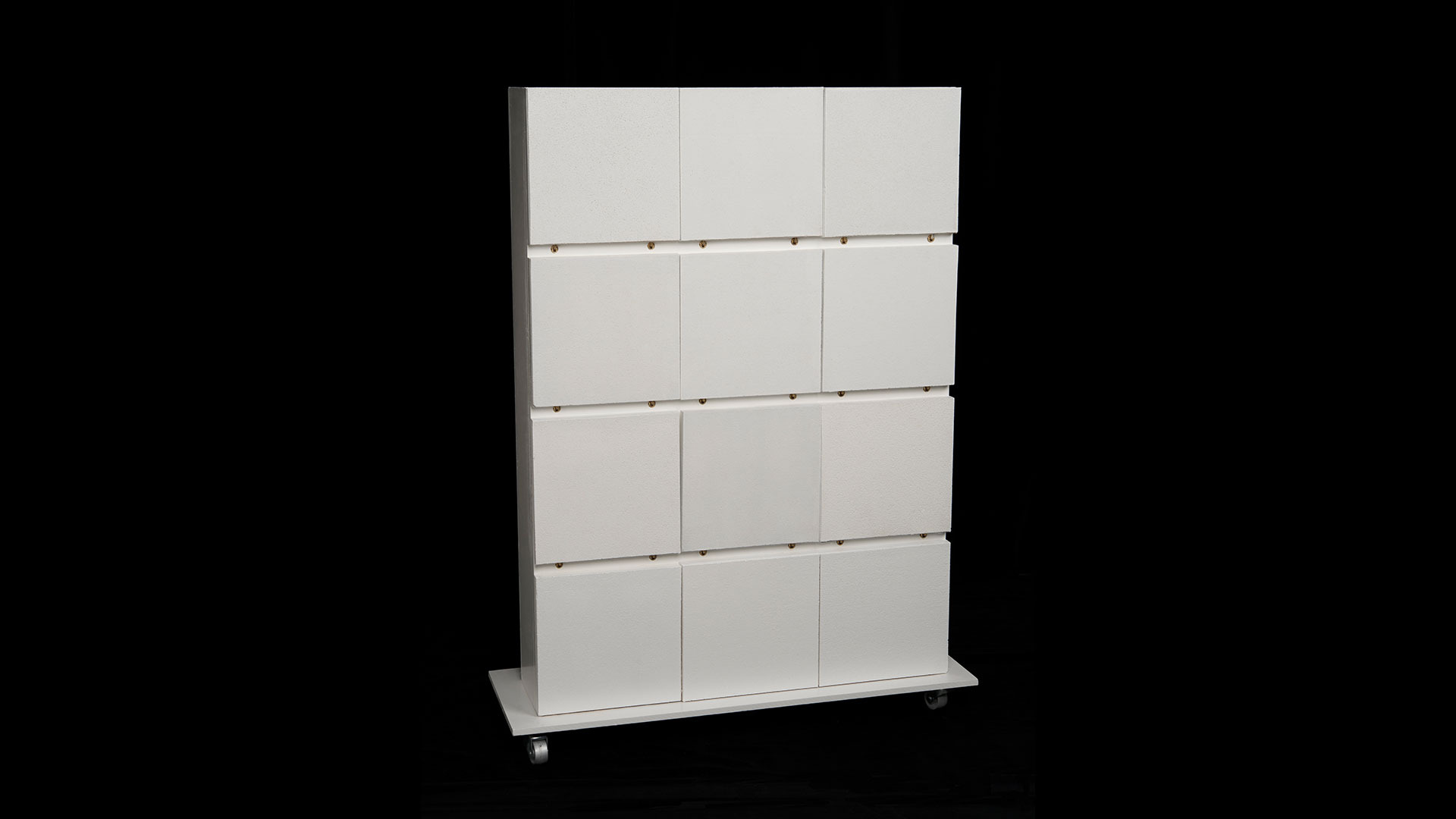 Standing wall of white squares, 3 squares wide and 4 squares tall, separated into distinct rows, all on top of a raised platform with wheels