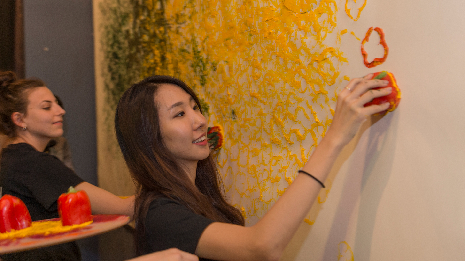 Student at white mural wall stamping red paint with cut bell pepper